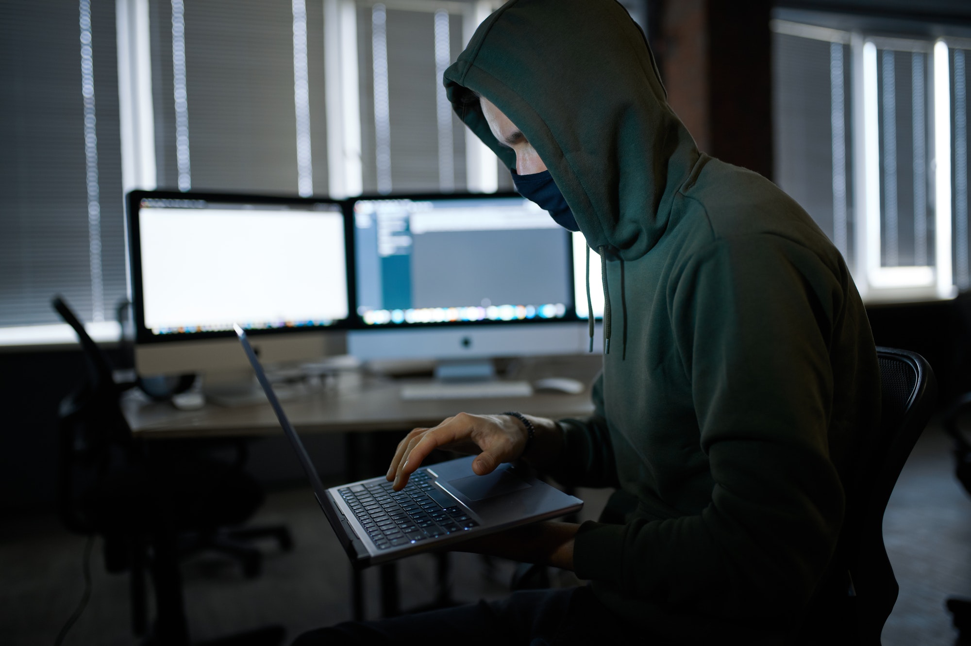Male hacker in hood holds laptop, front view